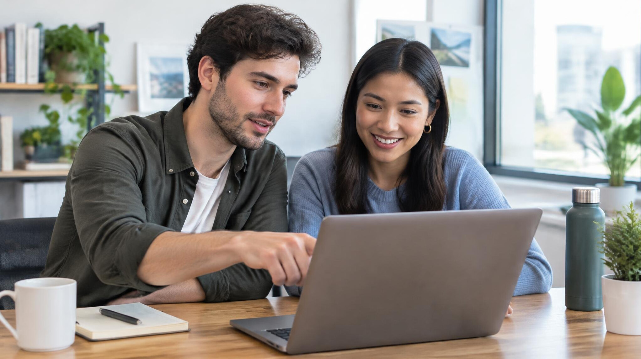 Two colleagues collaborating on a laptop at a wooden desk